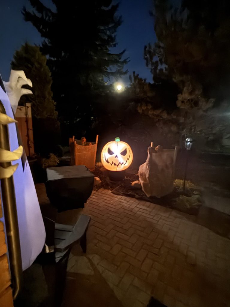 A lit jack-o’-lantern on a dark front walk under the moon