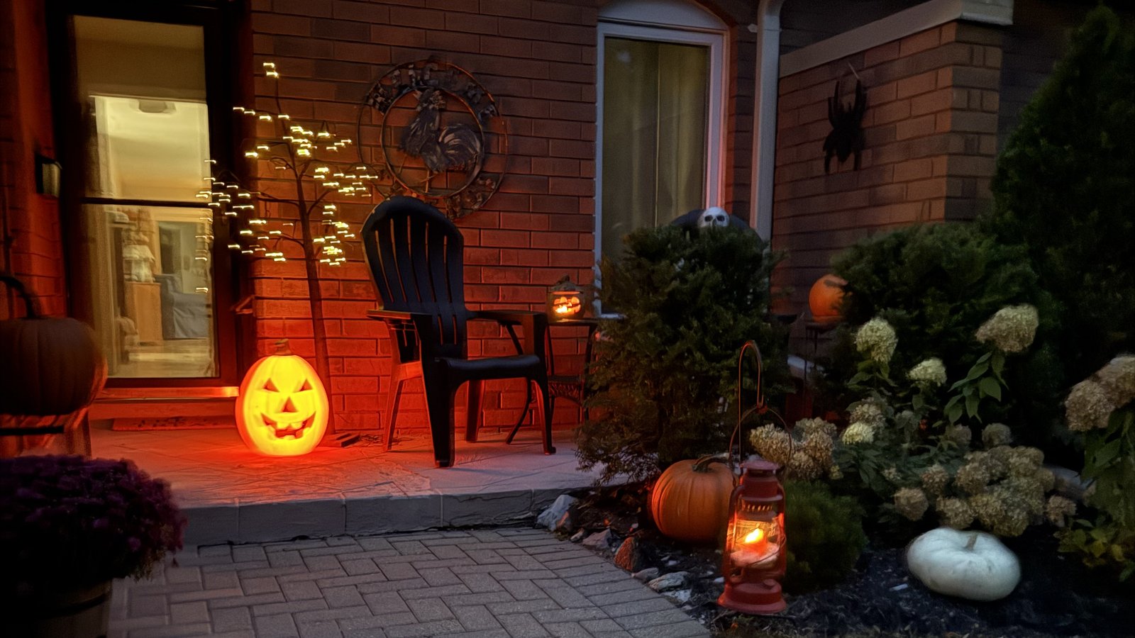 Front porch in Lakefield at dusk with a glowing jack-o’-lantern, lantern and pumpkins